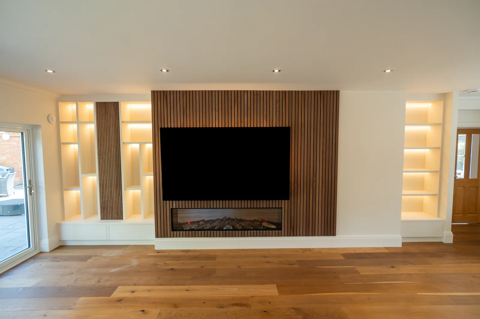 Timber slat media wall with fireplace and illuminated white shelving on either side