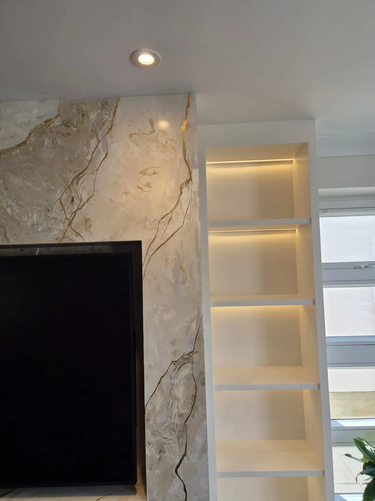 Close up of hand applied Venetian plaster with gold veining on the return edge of a media wall panel, next to a backlit shelf column