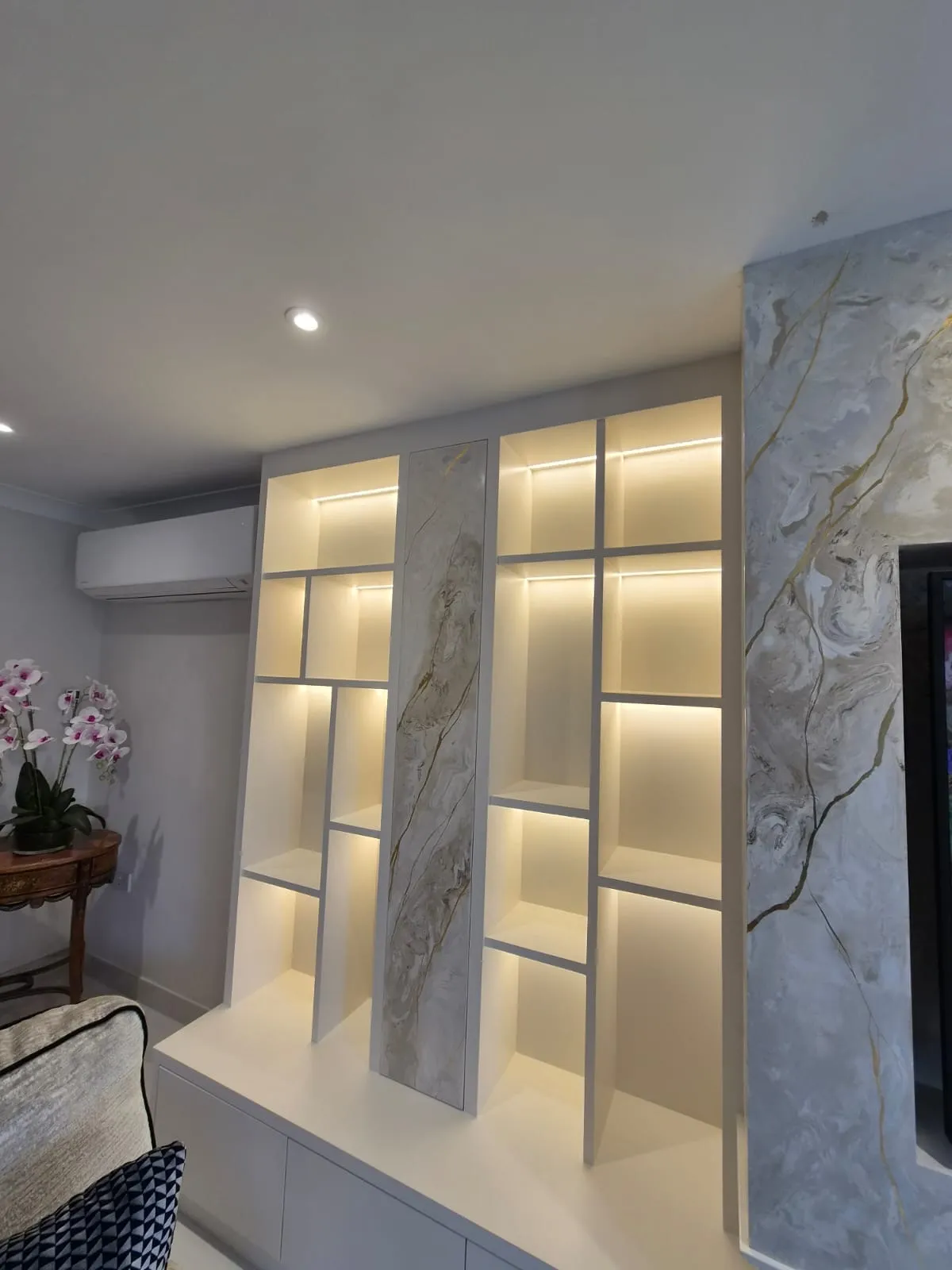 Backlit geometric shelving with a vertical Venetian plaster panel running through the middle, part of a bespoke media wall